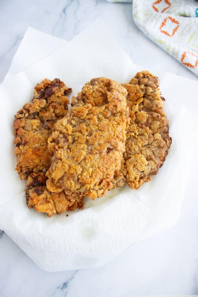 Chicken fried steak drying on a paper towel lined plate.