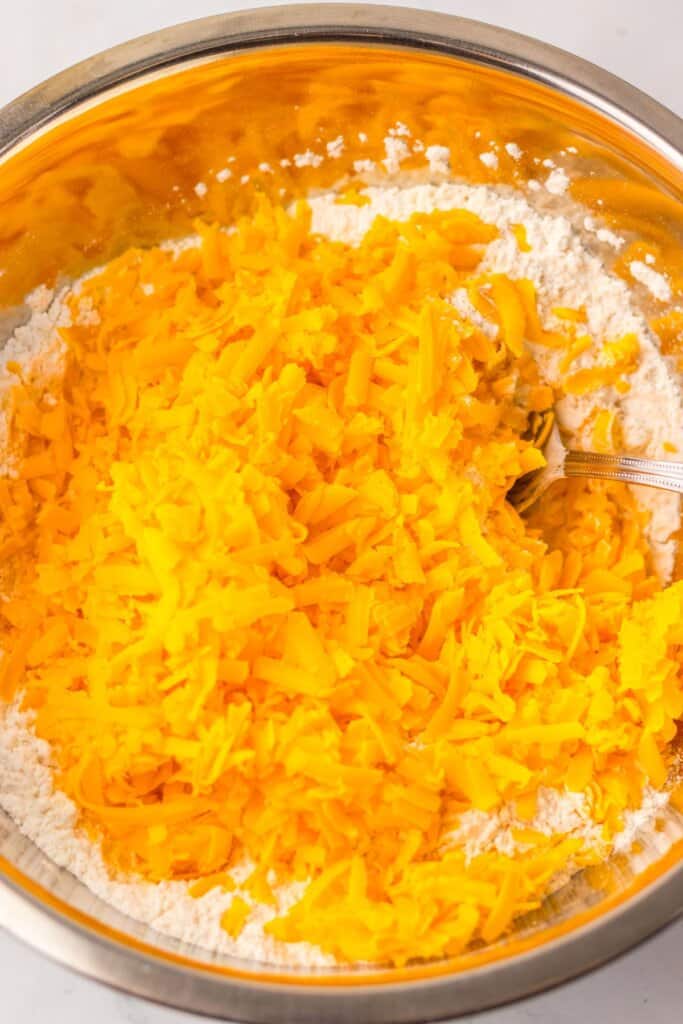 Cheese being added to a stainless steel mixing bowl.