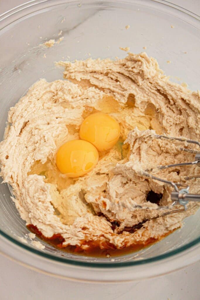Eggs being added to butter and sugar in a large bowl.