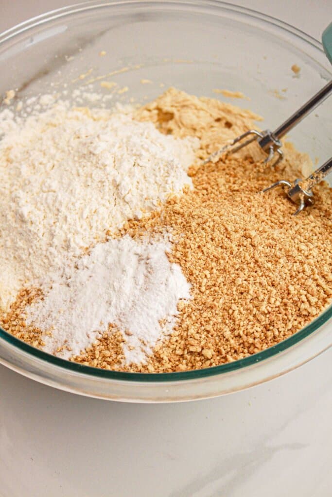 Dry ingredients being added to wet ingredients in a large glass mixing bowl.