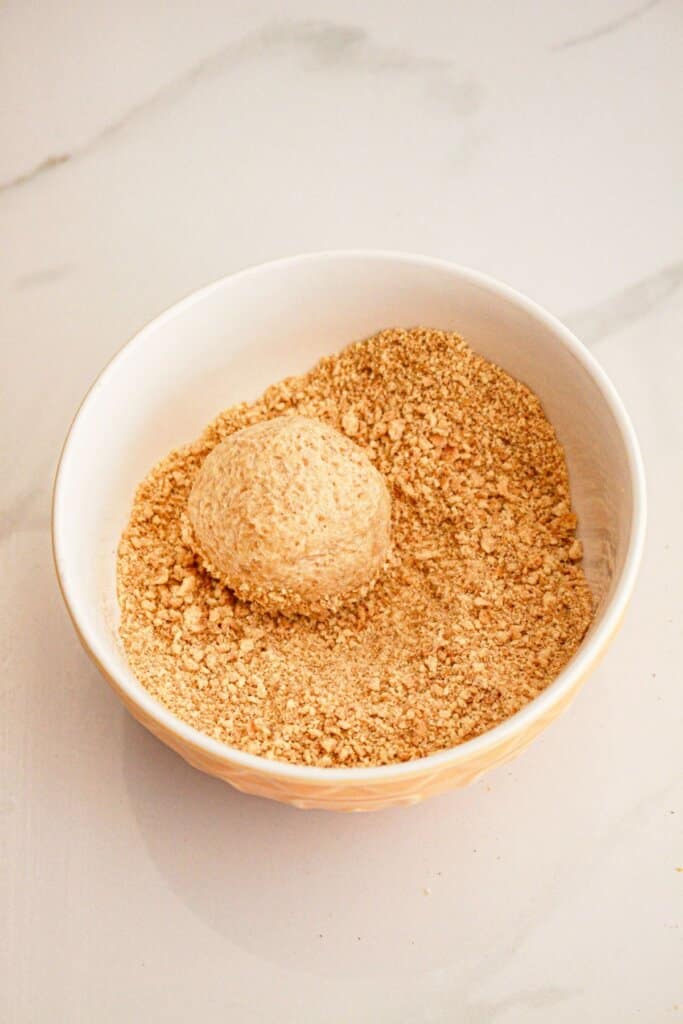 Dough ball being rolled in graham cracker crumbs.