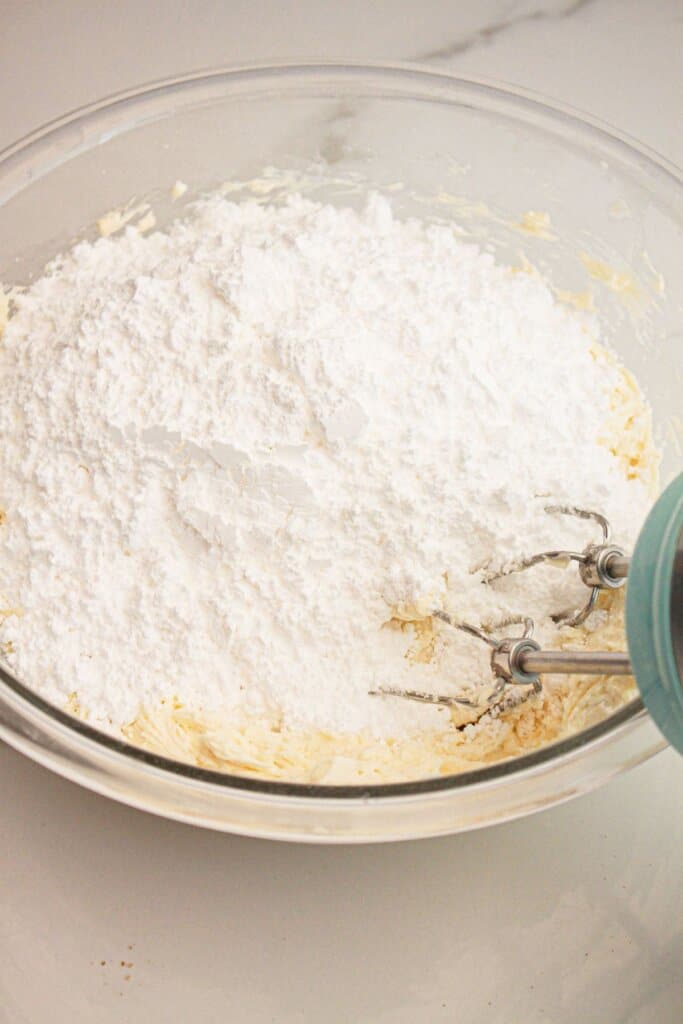 Powdered sugar being mixed with butter in a large glass bowl.