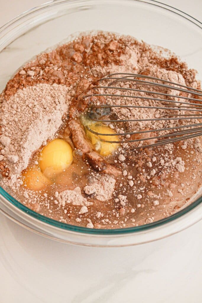 Cake mix, eggs, oil, and water being mixed in a glass bowl.
