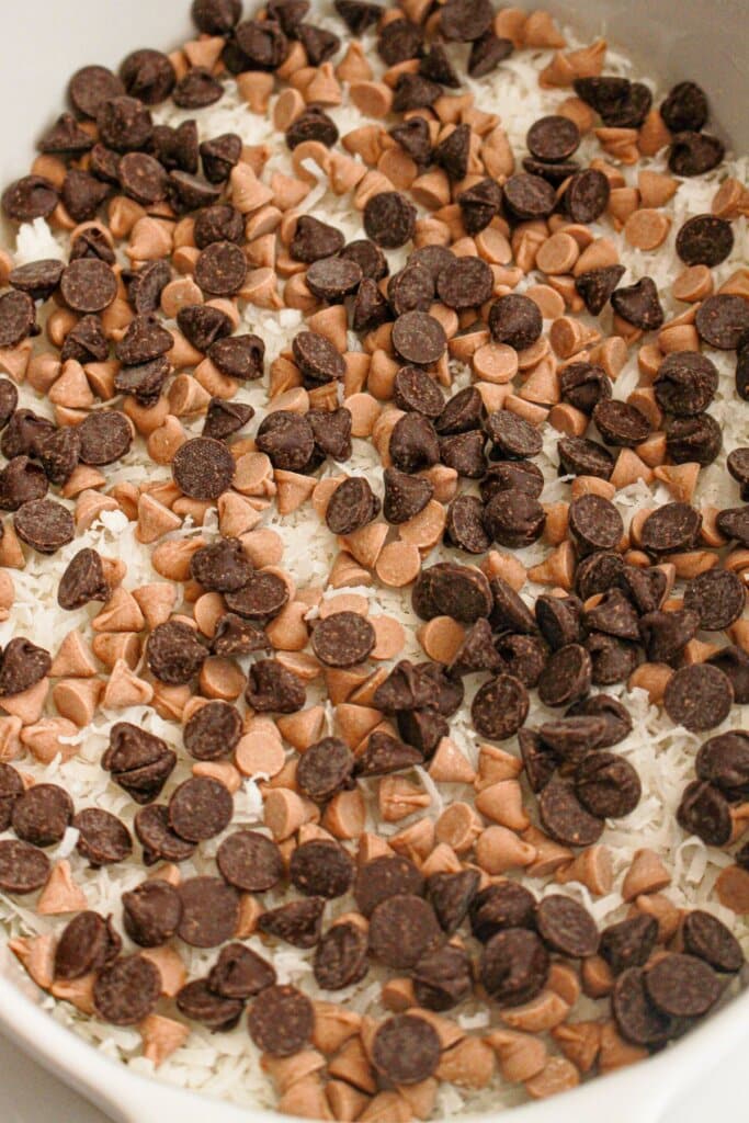 Chocolate chips, caramel chips and coconut in a white baking dish.