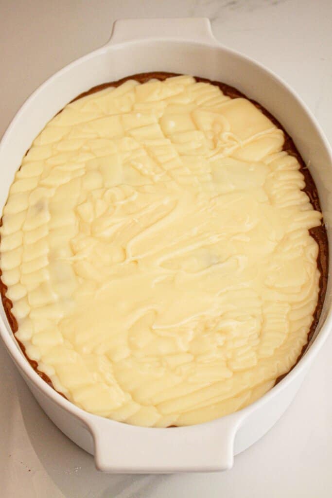 Cream cheese being spread on top of dessert in a baking dish.
