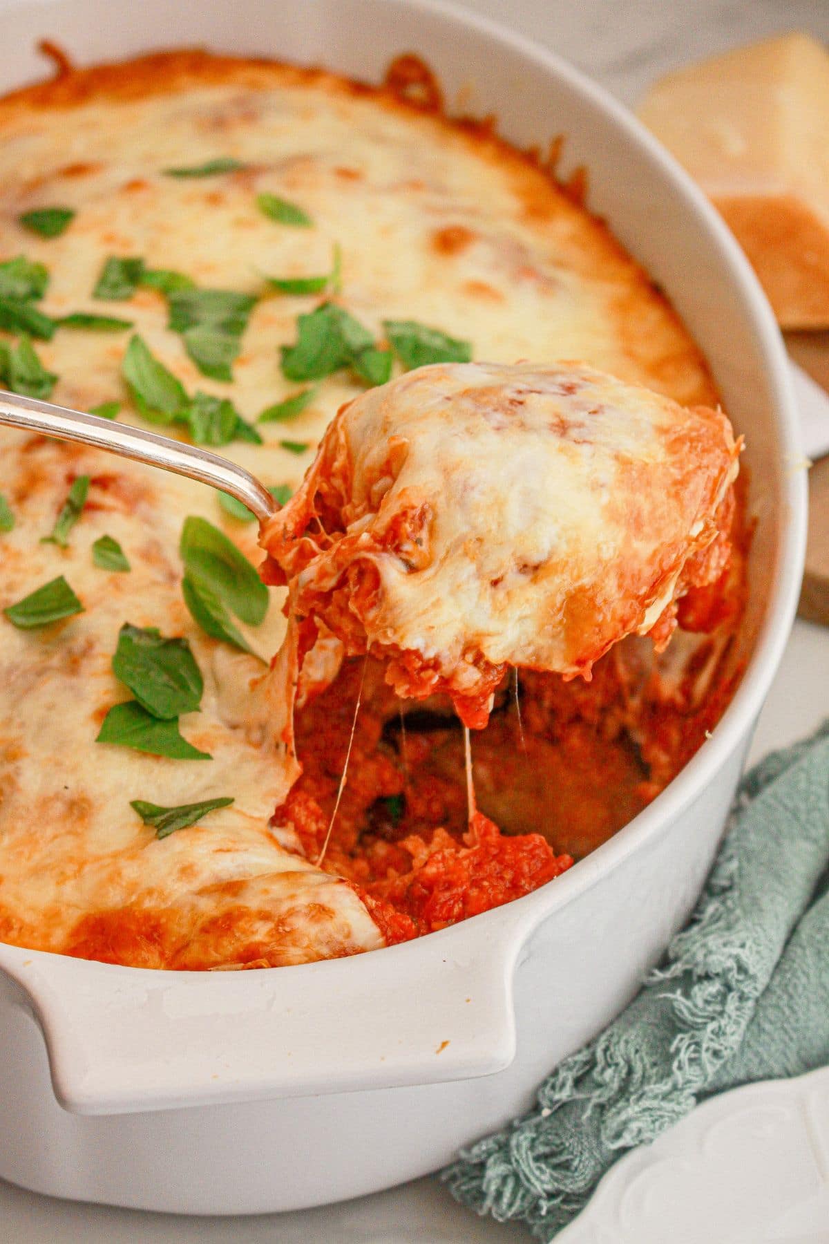 Scoop of eggplant parmesan being removed from a baking dish.