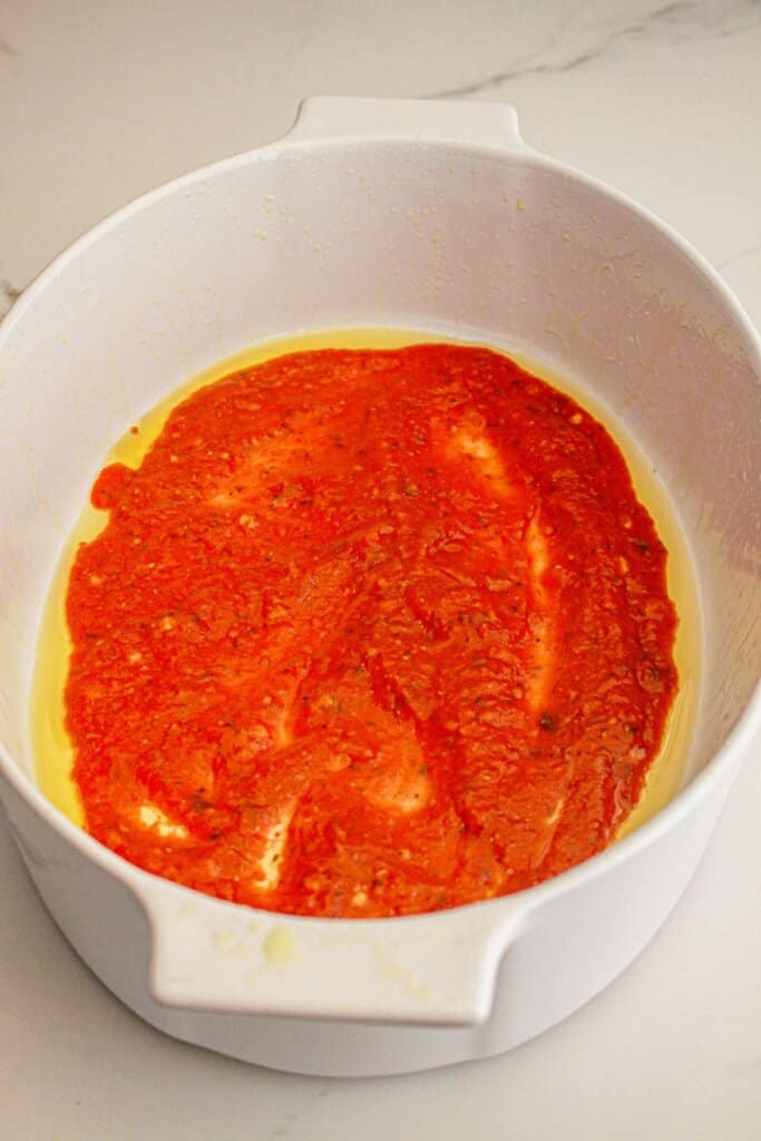 Sauce being spread into the bottom of a baking dish.