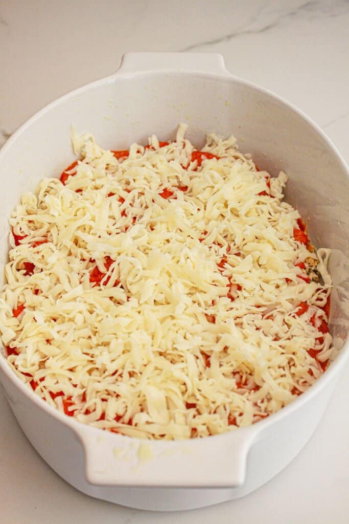 Shredded cheese on top of sauce in a baking dish.