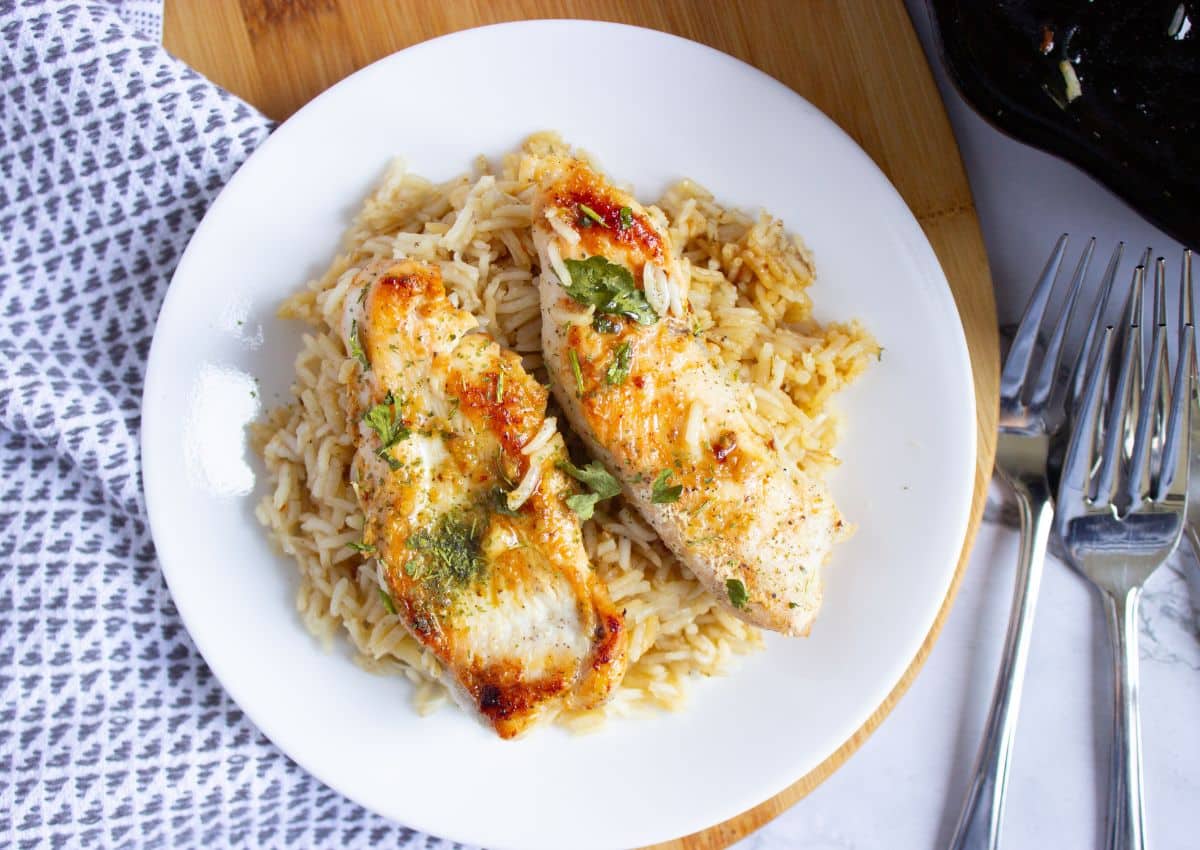 Plate full of rice with two chicken tenderloins on top.