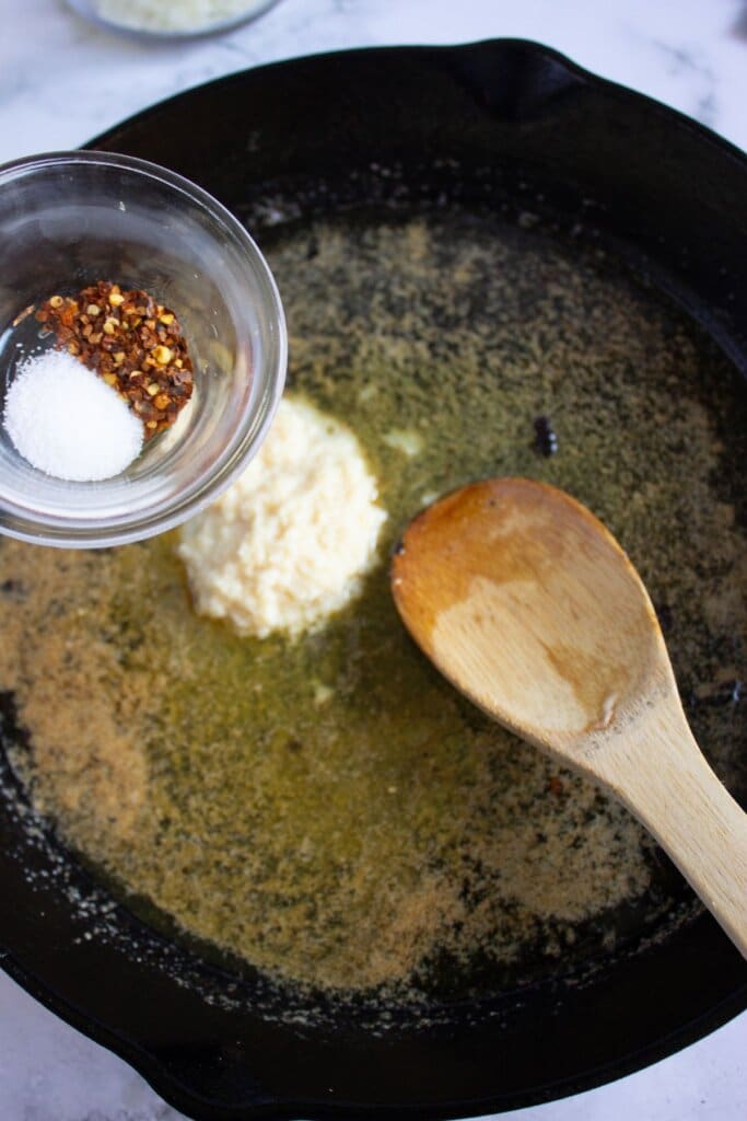 Salt and red pepper flakes being added to a cast iron skillet.