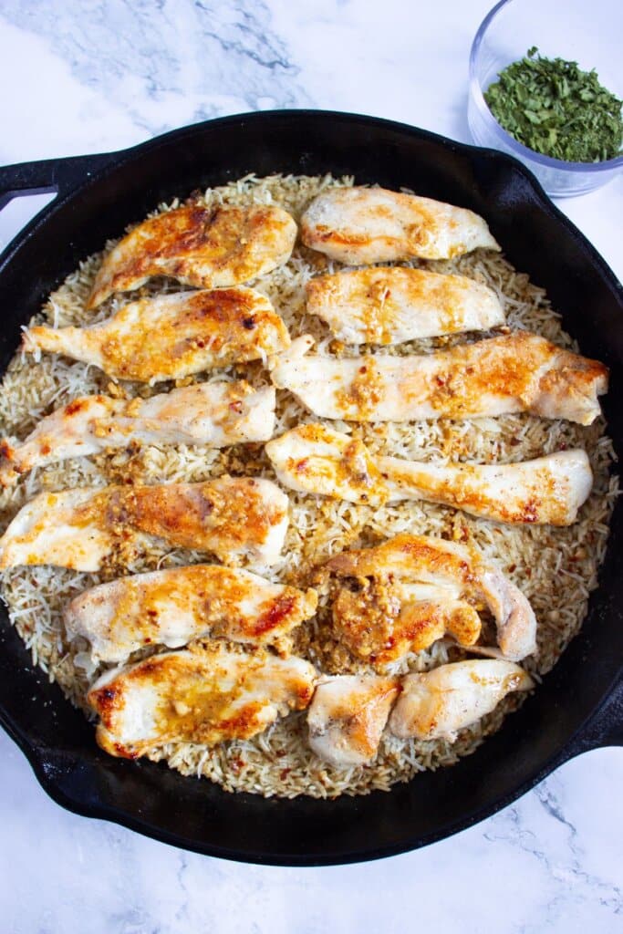 Sauce being drizzled over the chicken tenders in a cast iron skillet.