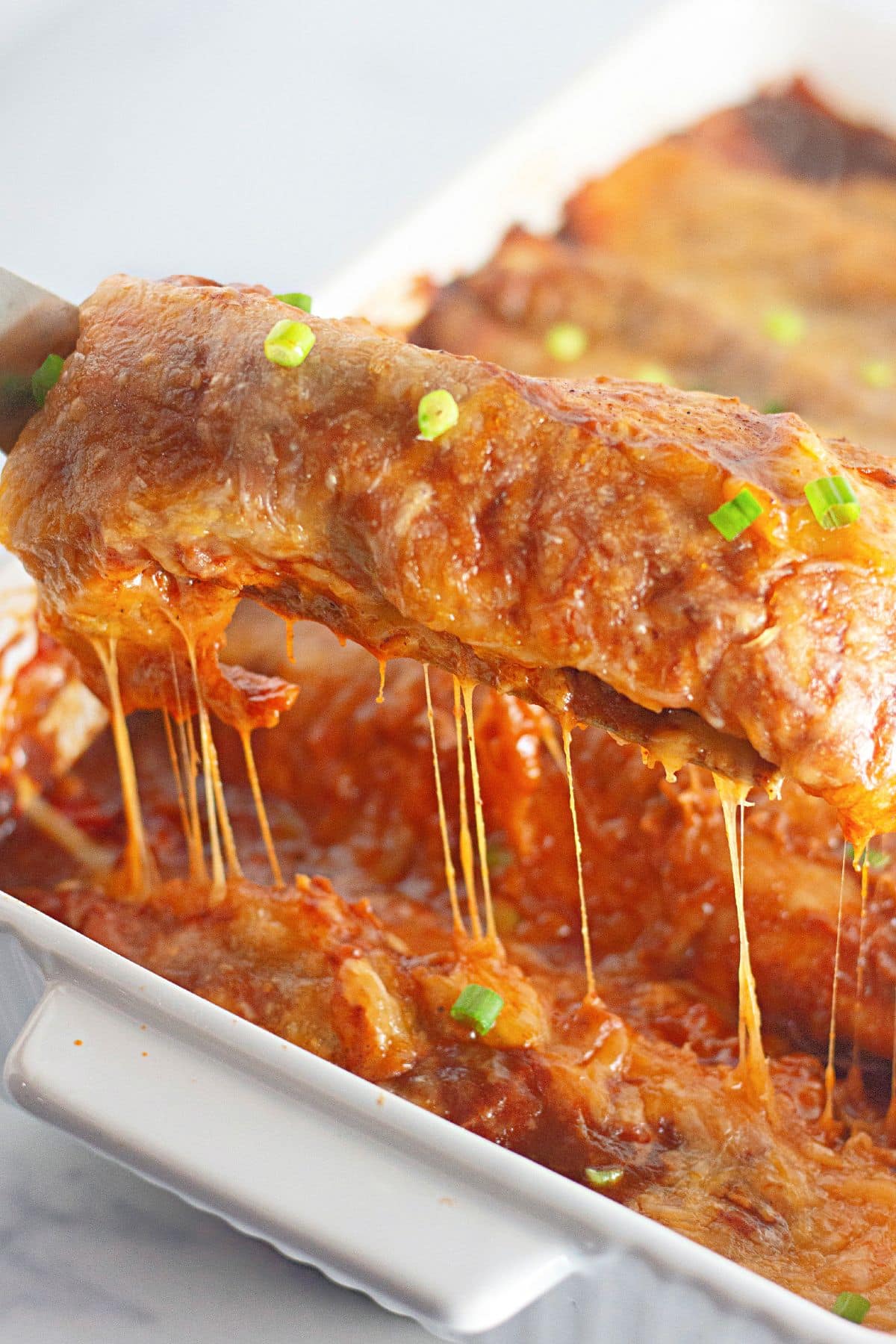 Ground beef enchilada being removed from a casserole dish.