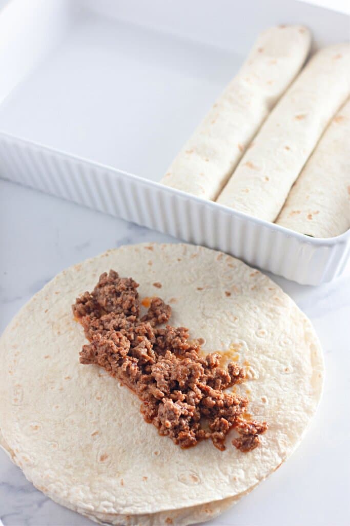 Taco meat being added to the center of a flour tortilla.