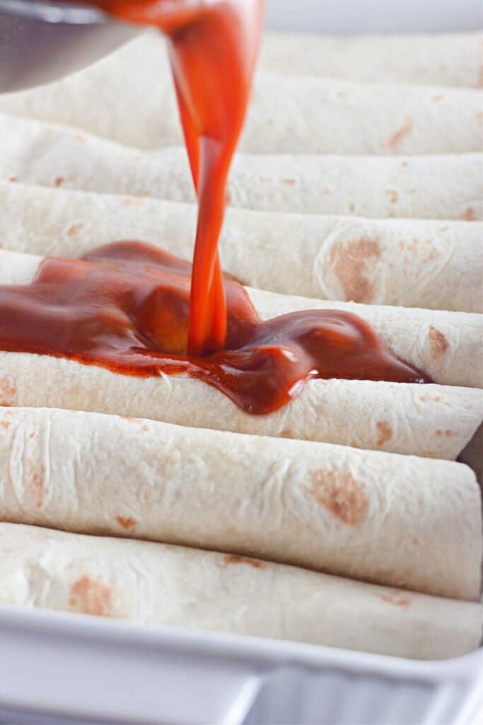 Sauce being poured over tortillas in a baking dish.