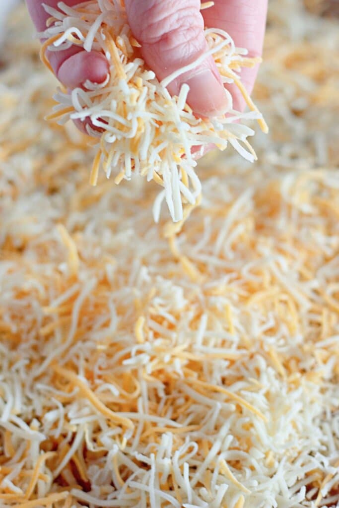 Shredded cheese being sprinkled on top of a baking dish.