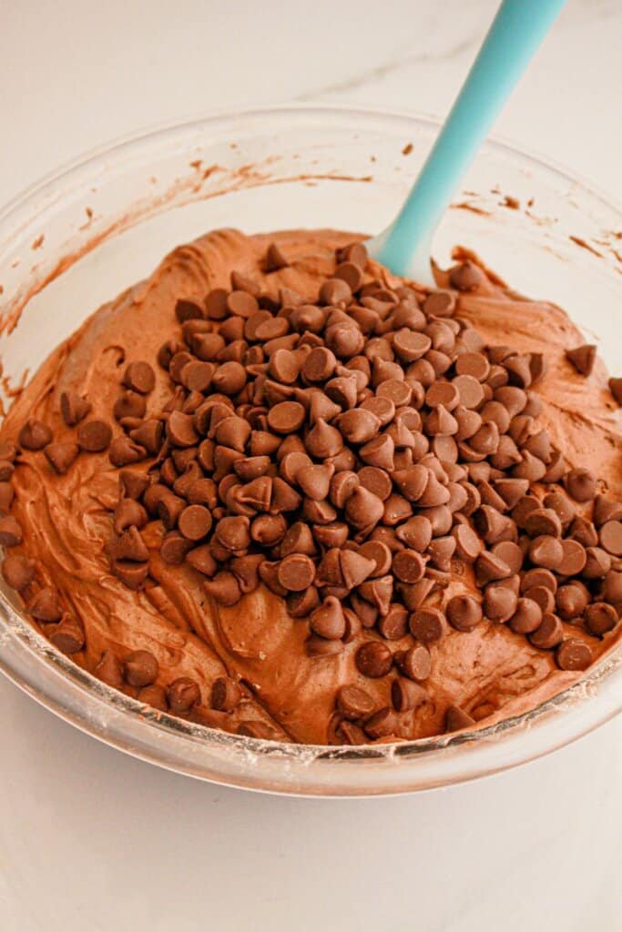 Chocolate chips being added to batter in a large mixing bowl.
