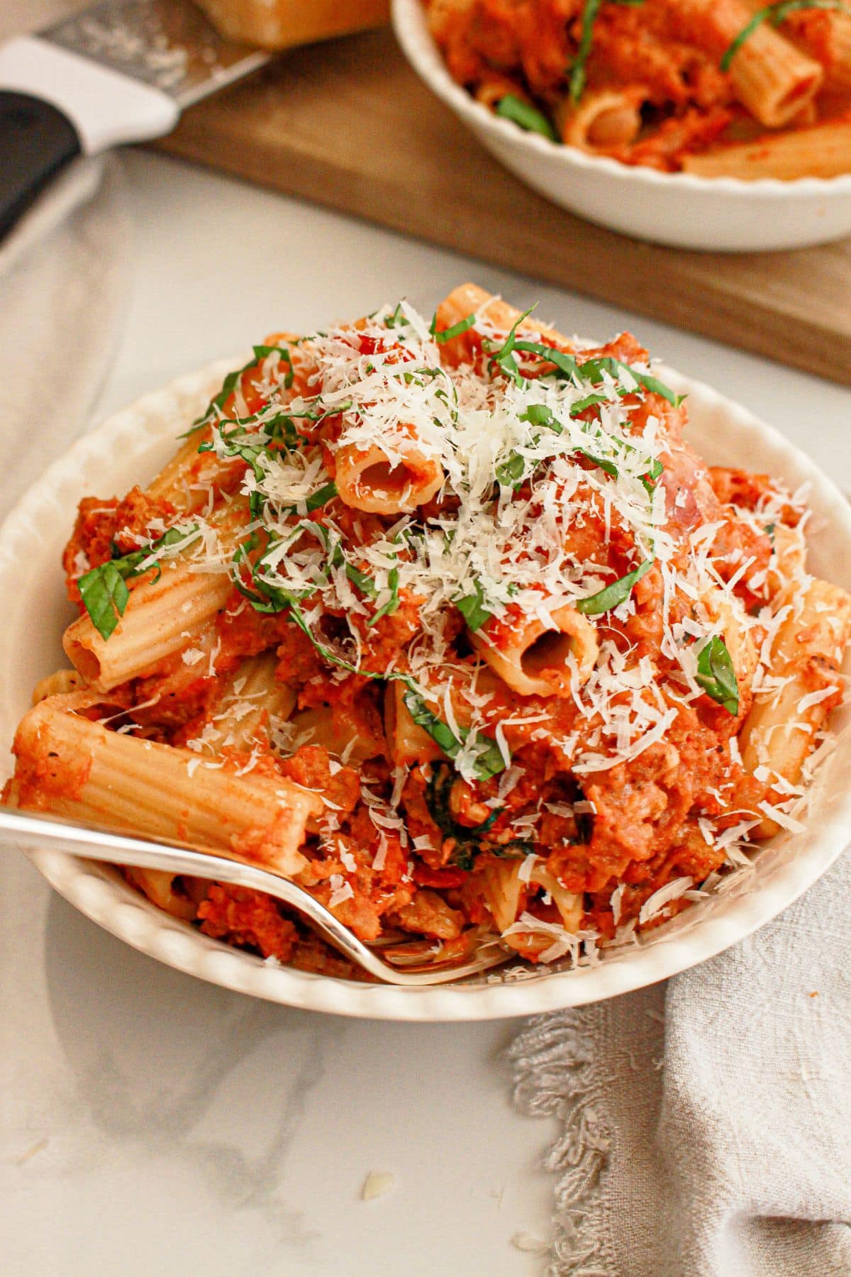 White bowl full of rigatoni and topped with grated parmesan cheese.