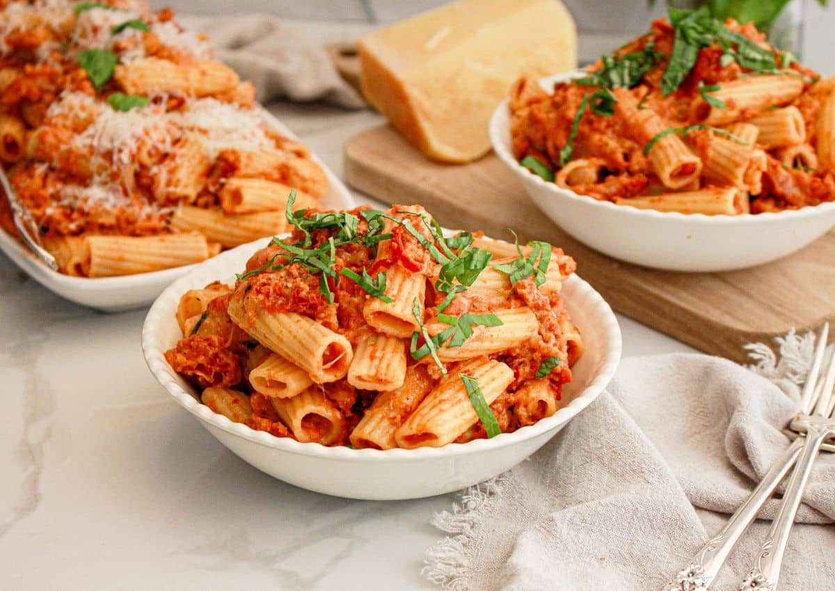 Two white bowls full of rigatoni with sausage.