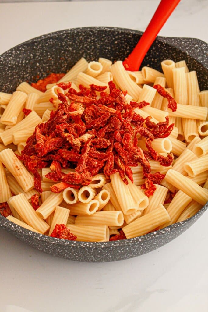 Sundried tomatoes and pasta being added to a pot.