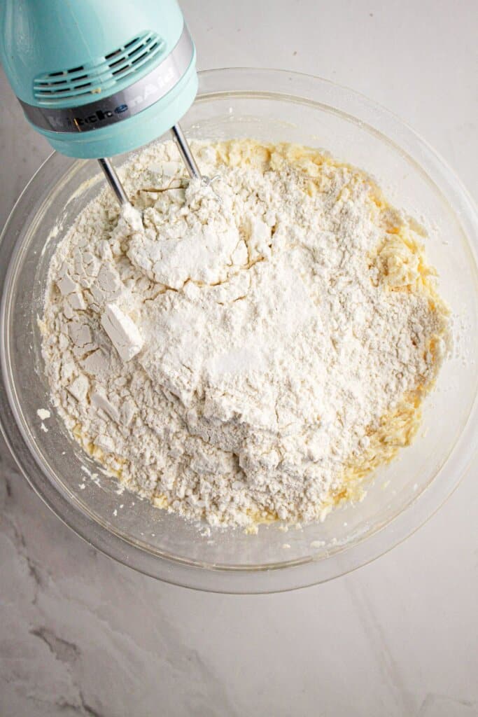 Dry ingredients being added to wet ingredients in a large glass bowl.