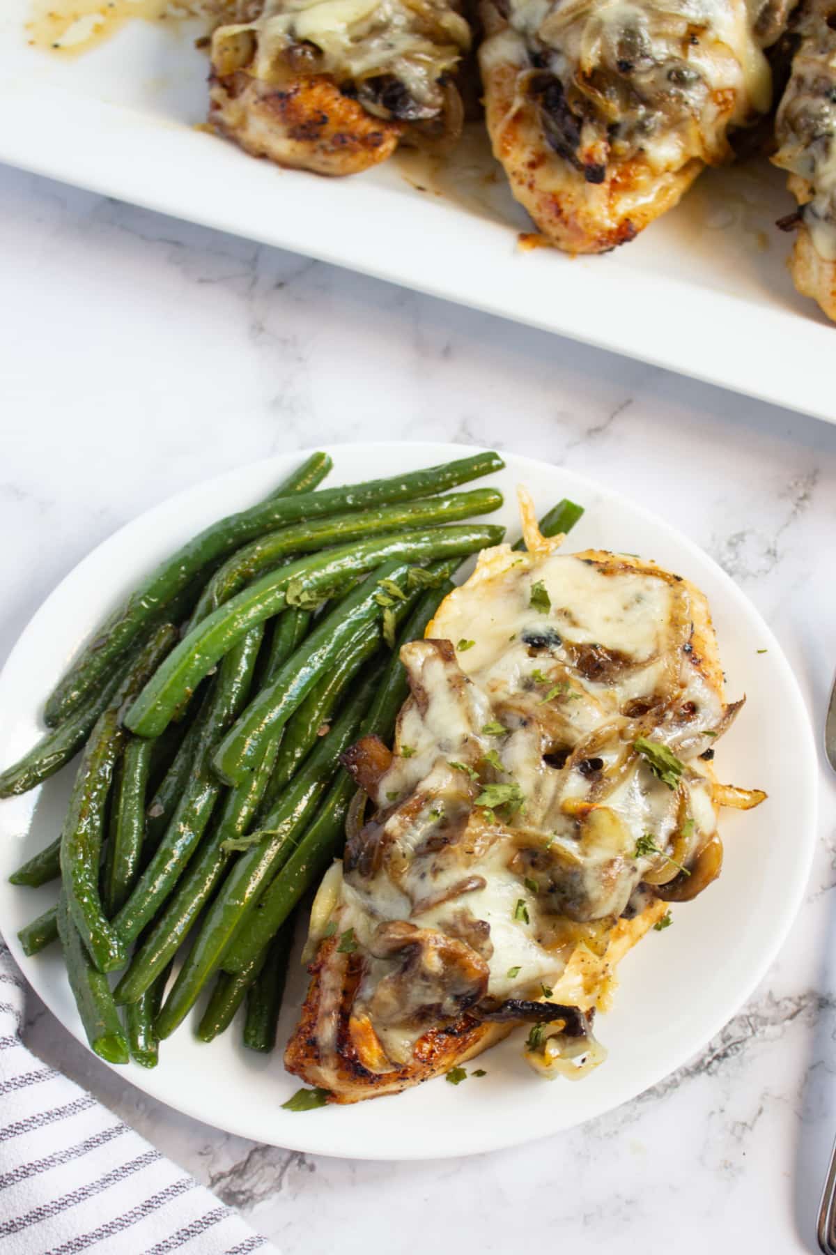 Piece of smothered chicken and green beans on a plate.