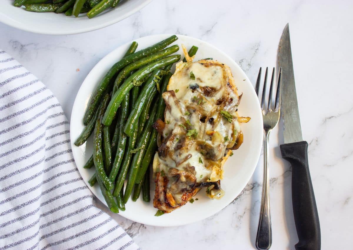 Piece of smothered chicken and green beans on a plate.