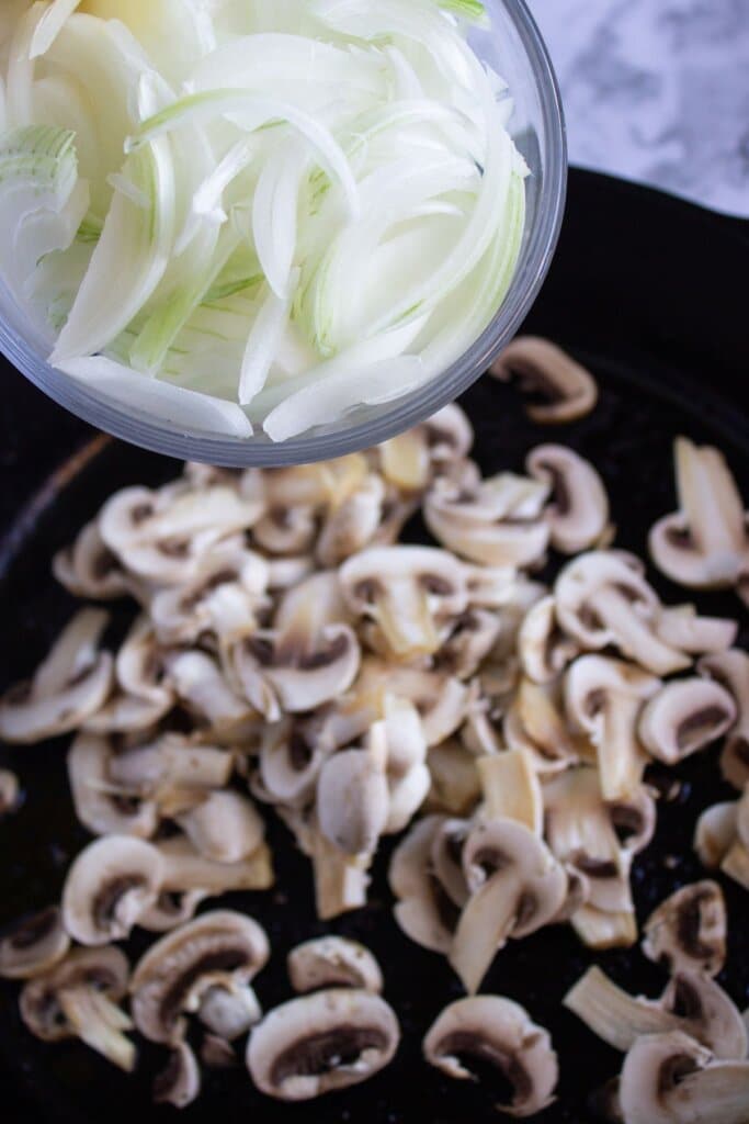 Onions being added to a cast iron skillet.