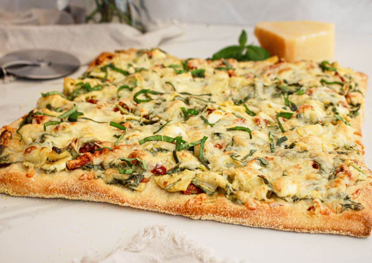 Spinach artichoke pizza on a counter ready to cut.