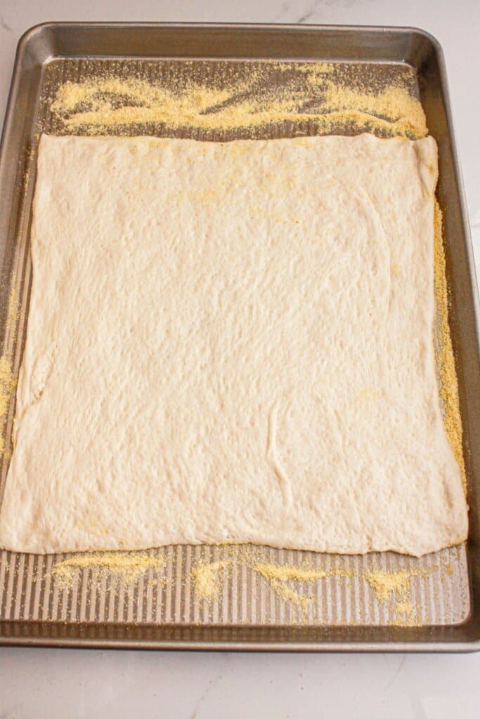 Pizza crust spread out on a baking sheet.