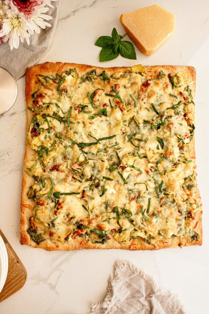 Spinach artichoke pizza on a counter ready to cut.