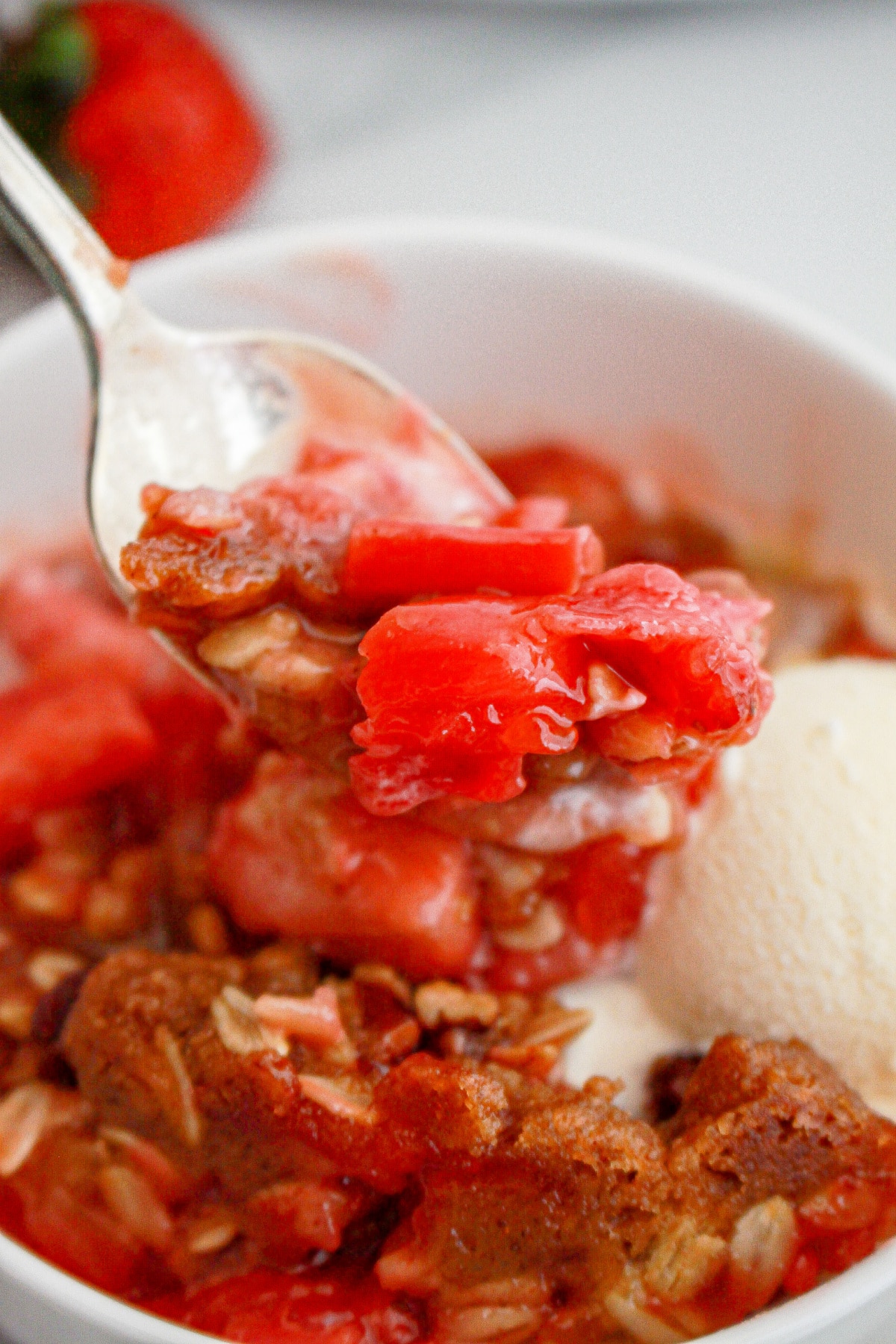 Serving of strawberry rhubarb crisp in a white bowl topped with a scoop of ice cream.