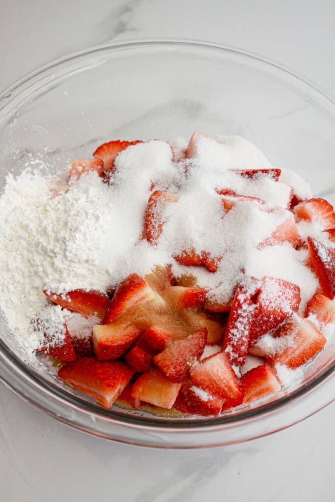 Strawberries and rhubarbs in a glass bowl with sugar.