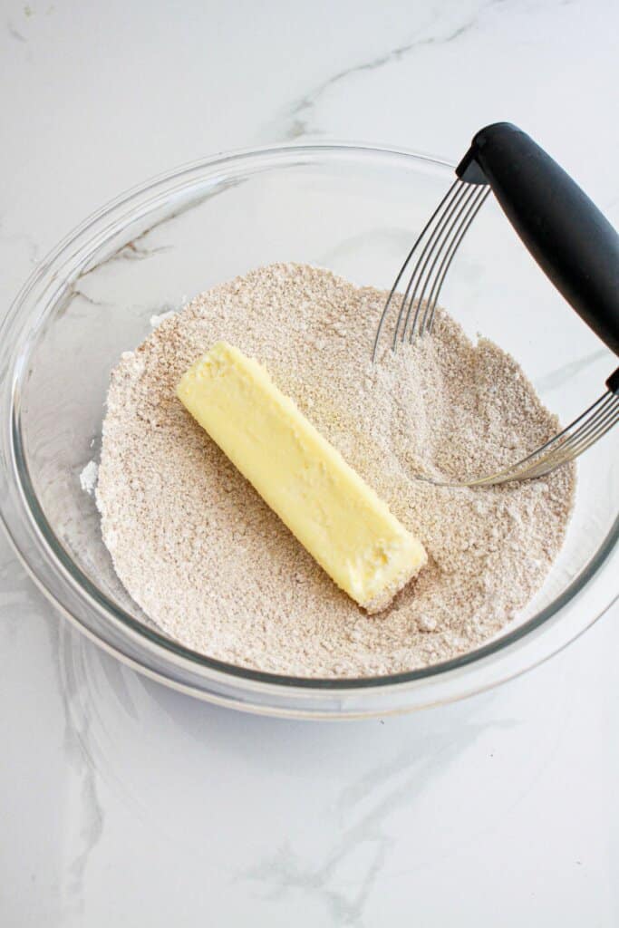 Butter being cut into brown sugar and flour in a glass bowl.