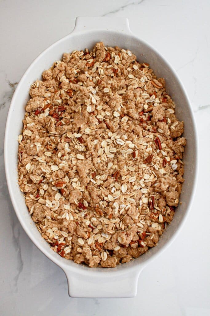 Crust being sprinkled on dessert in a white baking dish.
