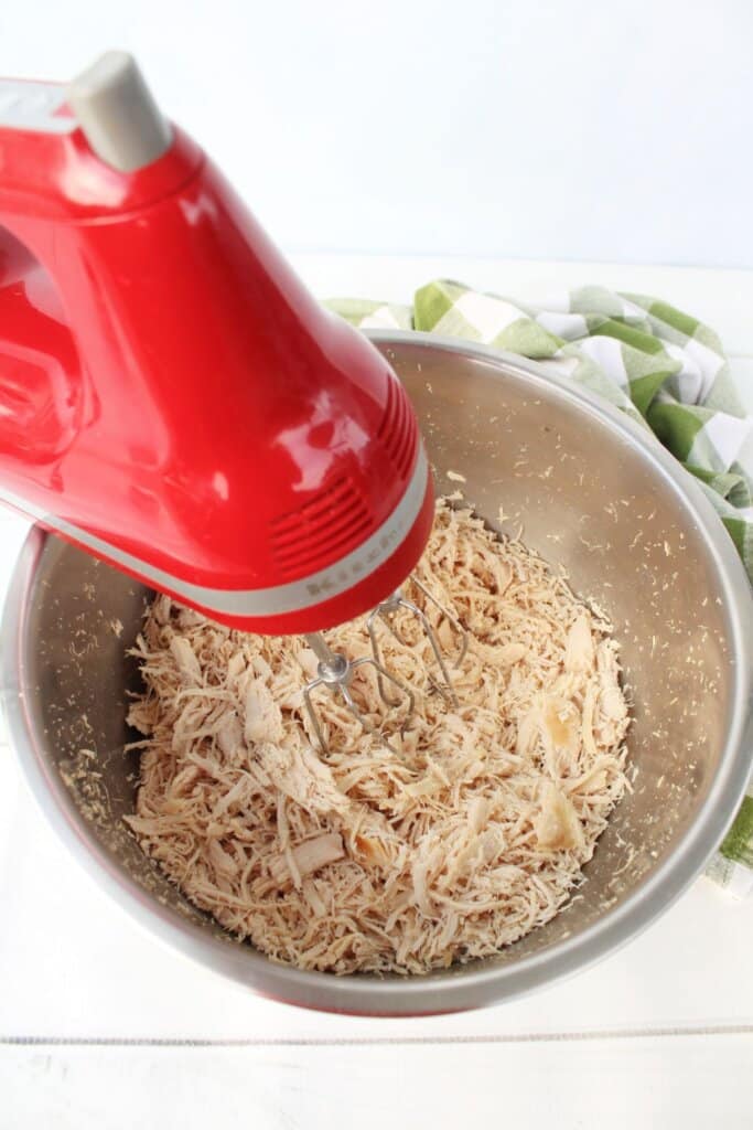 Chicken being shredded in a mixing bowl.