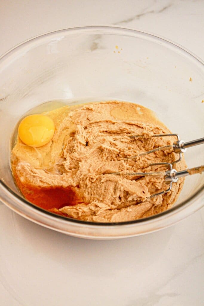 Eggs and vanilla being added to dough in a glass bowl.