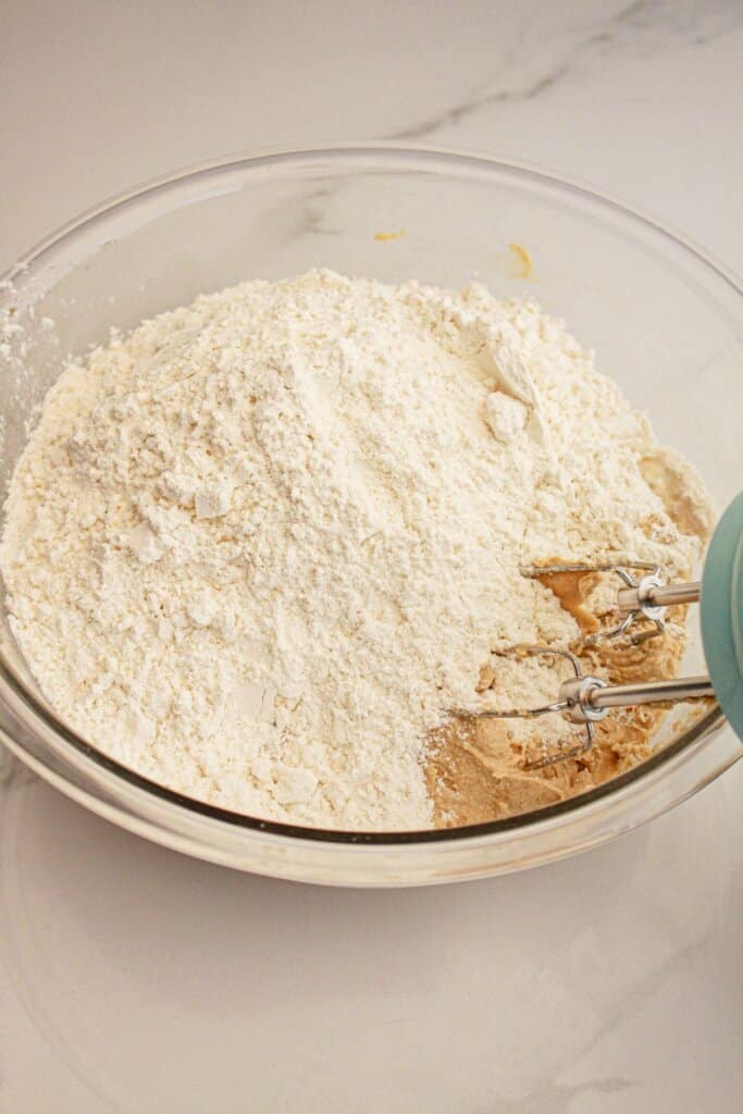 Dry ingredients being added to dough in a glass mixing bowl.
