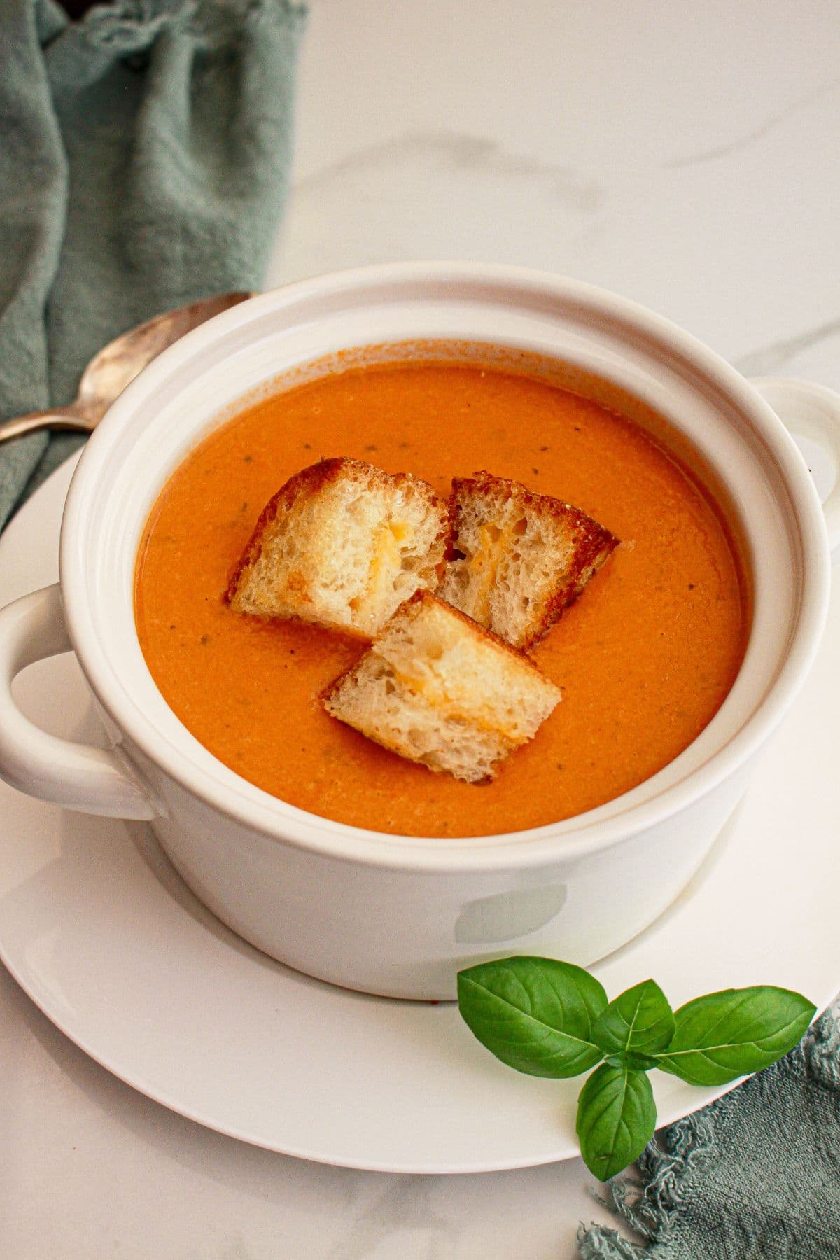 Bowl of tomato soup with three grilled cheese pieces inside of it.