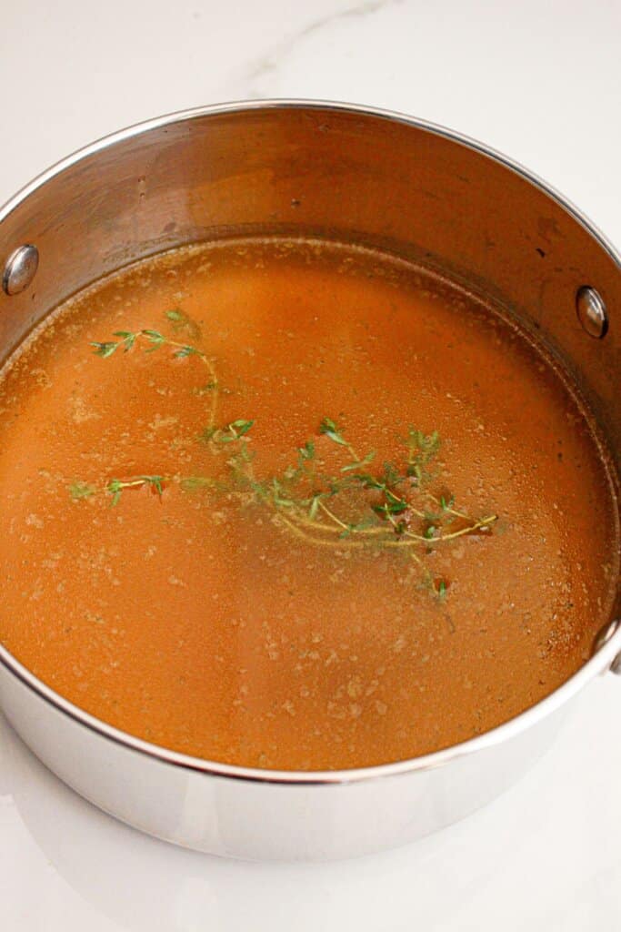 Broth and herbs in a large stainless steel pot.