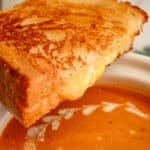 Half of a grilled cheese sandwich on top of a bowl of soup.