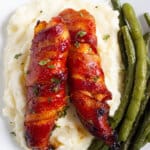 Bacon wrapped chicken tenders on top of mashed potatoes with a side of green beans.