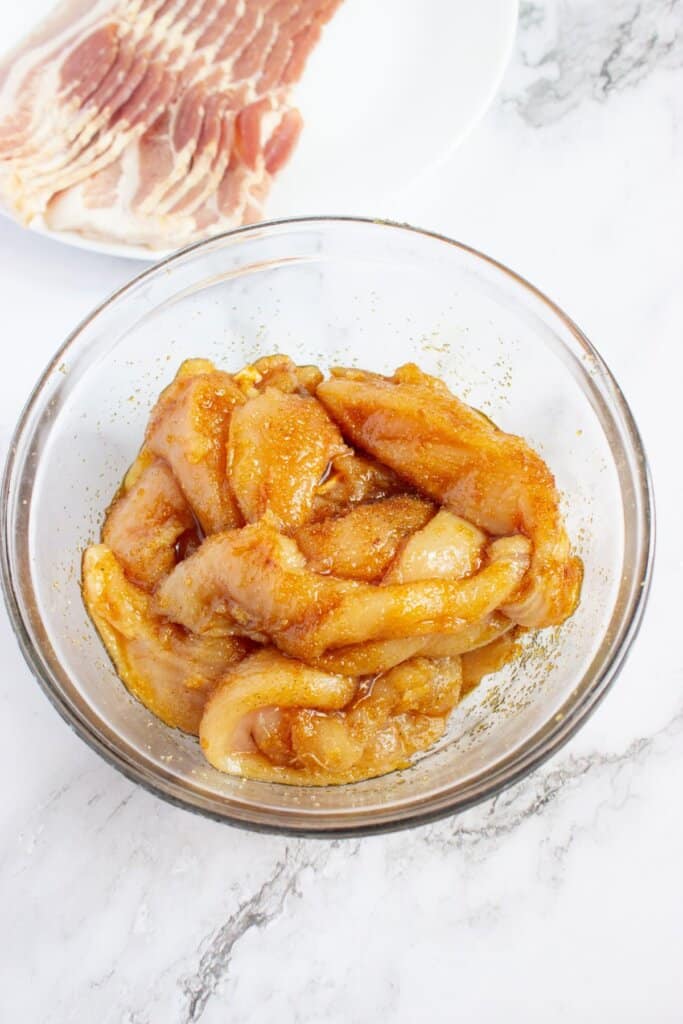 Chicken being coated in seasonings in a glass bowl.