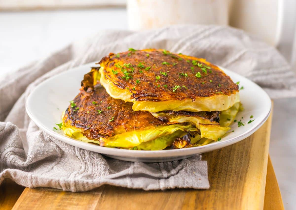 Parmesan cabbage steaks stacked on a white plate.
