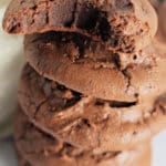 Brownie cookies stacked on top of each other next to a glass of milk.