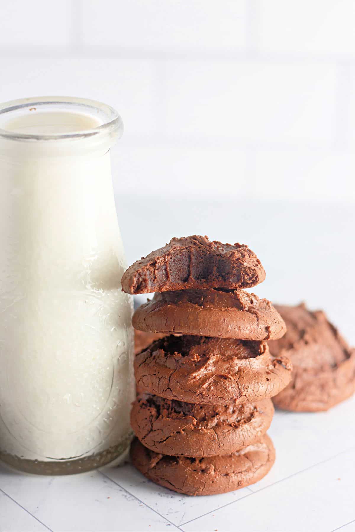 Brownie cookies stacked on top of each other next to a glass of milk.