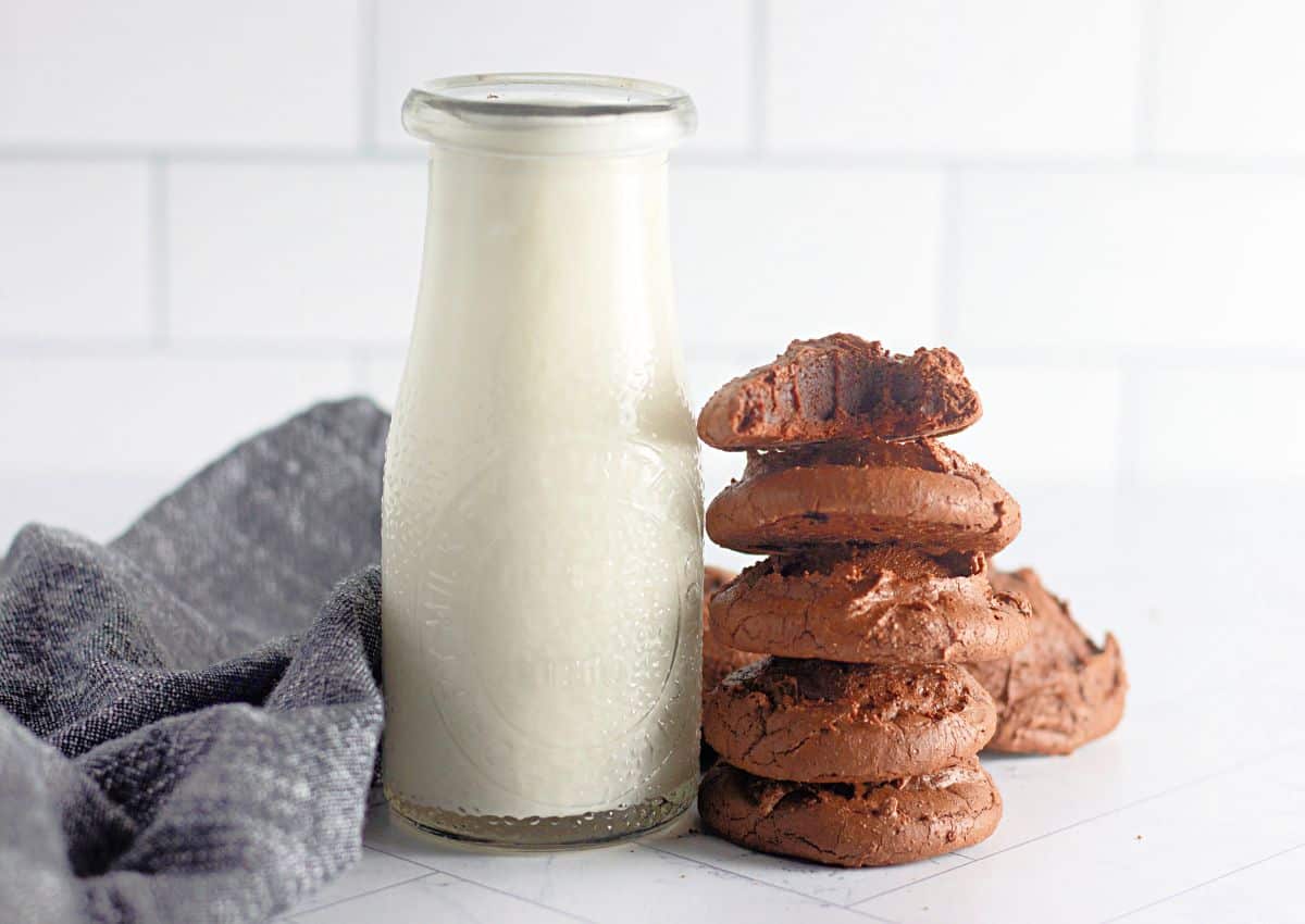 Brownie cookies stacked on top of each other next to a glass of milk.