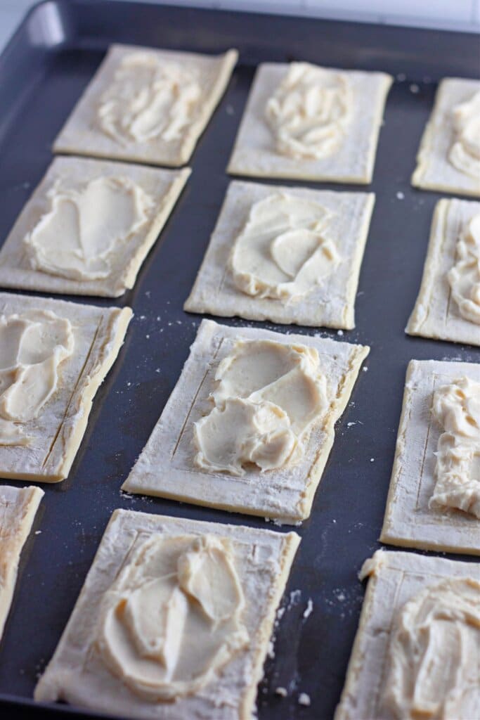 Cream cheese being spread on top of puff pastry.