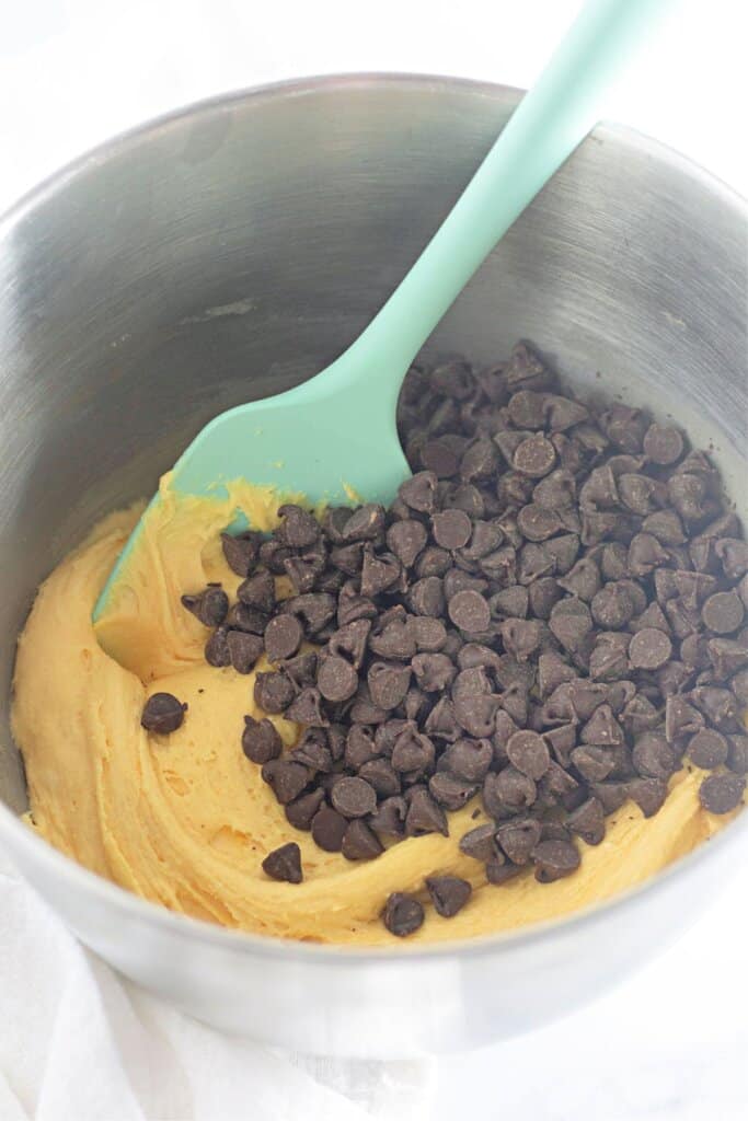 Chocolate chips being folded into dough in a mixing bowl,