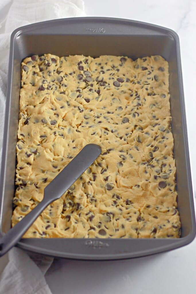 Cookie dough being spread into a baking dish.