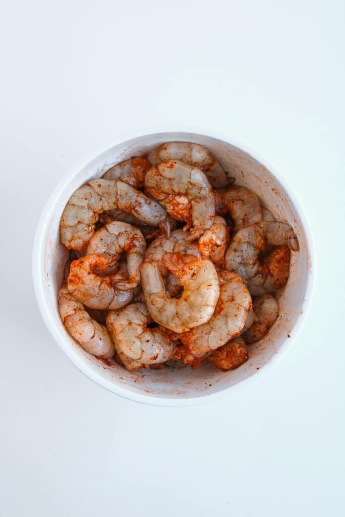 Shrimp being seasoned in a small bowl.